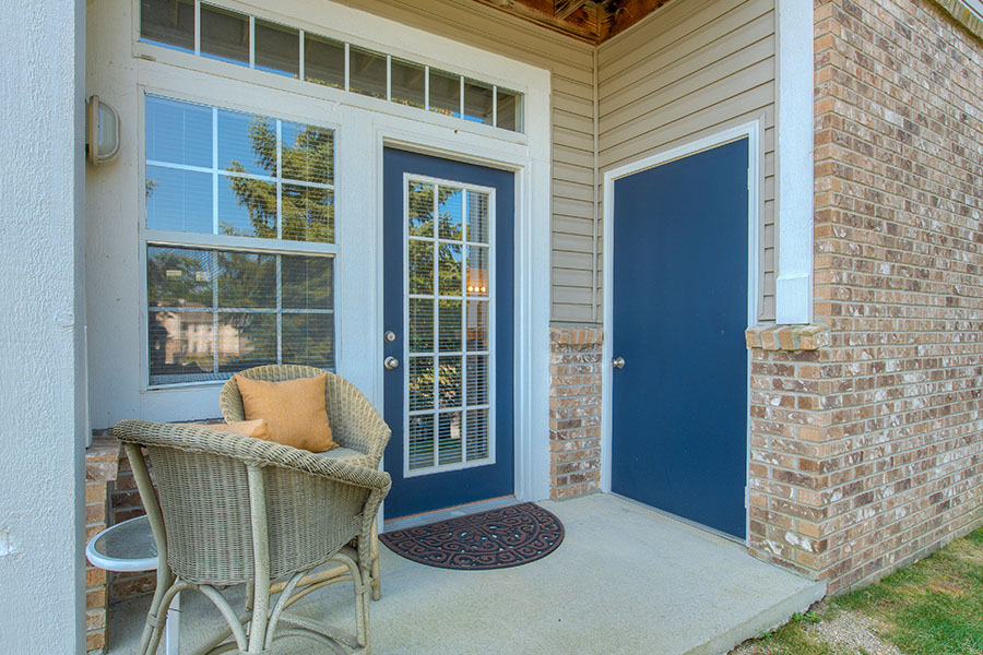 Welcoming mat and set of wicker chairs on a front porch of an apartment entryway located at Bayshore Apartments.